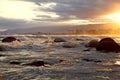 Sunset on beach and sea waves crashing dark rocks,