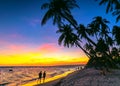 Sunset on the beach with silhouette couple, tilted coconut trees, Royalty Free Stock Photo