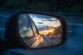 Sunset and beautiful sky is reflected in the mirror of a car. Cars drive along a high road in the evening. Theme of Royalty Free Stock Photo