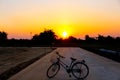 Sunset on beauty sky tree silhouette and single bicycle on concrete road the evening background