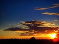 Sunset with blue sky and orange clouds illuminated by white sun and red fire glow on black tree wood