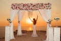 Sunset. bride silhouette. Wedding ceremony arch with flower arrangement and white curtain on cliff above sea, outdoor summer