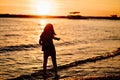 at sunset. kid girl walks along seashore, collects stones and throws into water Royalty Free Stock Photo