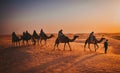 Sunset in desert with camel caravan silhouette on sand dunes.