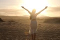 Sunset in the desert. Young woman with raised arms wearing white dress walking in the desert dunes sand during sunset. Girl on Royalty Free Stock Photo