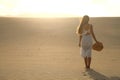 Sunset in the desert. Young woman with white dress walking in the desert dunes with footsteps in the sand during sunset. Girl