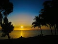 Sunset glow over a beautiful tropical beach and ocean water. Different colours of clouds and the silhouette of palm tree. Royalty Free Stock Photo