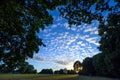 Sunset in Harvington Park, Beckenham, Kent. Small fluffy altocumulus clouds against a blue sky with the setting sun