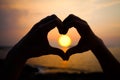 Sunset heart. Hand heart frame shape silhouette made against the sun and sky of a sunset on a deserted empty beach Royalty Free Stock Photo