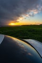 Sunset on the horizon with golden clouds and reflections on the glass of a car in the foreground.