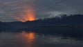 Sunset on the lake with sun setting and creating cone of light emerging from the mountain