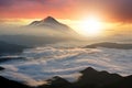 Sunset landscape with high peaks and foggy valley with thick white clouds under vibrant colorful evening sky in rocky mountains Royalty Free Stock Photo