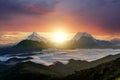 Sunset landscape with high peaks and foggy valley with thick white clouds under vibrant colorful evening sky in rocky mountains Royalty Free Stock Photo