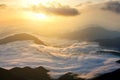 Sunset landscape with high peaks and foggy valley with thick white clouds under vibrant colorful evening sky in rocky mountains Royalty Free Stock Photo