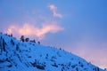 The sunset light hits a wispy cloud over a snowy mountain