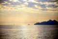 Sunset light on an isolated sailboat, sailing on the horizon, with the coast in backlight, under a dramatic sky Royalty Free Stock Photo