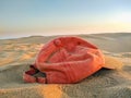 sunset light of a red cap abandoned or forgotten on the brown sand of dune of the desert by a tourist person on holidays. The wind