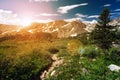 Sunset light shining behind a distant mountain range and a dirt hiking trail winding through an alpine meadow in Colorado Royalty Free Stock Photo