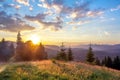 Sunset in the mountains, glade with green grass in the rays of the sun, the landscape in backlight Royalty Free Stock Photo