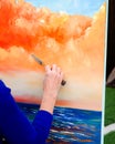 Sunset ocean sky painted by senior lady artist hand holding palette knife finishing up colorful abstract on easel canvas stand, Royalty Free Stock Photo