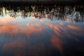 Sunset orange clouds and trees silhouettes reflected on water surface