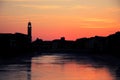 Sunset over black silhouette of Pisa cityline and Aron river