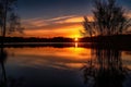 sunset over calm lake, with water reflections and silhouettes of trees