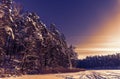 Sunset over the frozen lake and pine forest. Footsteps tracks on the snow Royalty Free Stock Photo