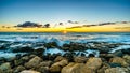 Sunset over the horizon with a few clouds and the rocky shores of the west coast of Oahu