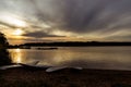 Sunset over a lake with paddle boards on the sandy shore with silhouette view of trees on horizon Royalty Free Stock Photo