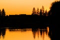 Sunset over the lake. Silhouettes of houses and trees in the rays of the evening sun. Black contours on orange background. Royalty Free Stock Photo