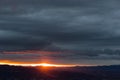 Sunset over mountains and valley, with sun coming down through an hole in the clouds