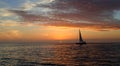 Sunset over the ocean with a sailboat sailing near the sun