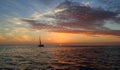 Sunset over the ocean with a sailboat sailing near the sun