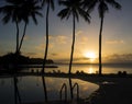 Sunset over pool and beach with clouds reflected in pool and trees in silhouette Royalty Free Stock Photo