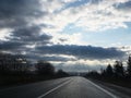 Sunset over the road. Blue white and yellow sky with dark clouds and sun rays before the rain. Travel ride by car around the Royalty Free Stock Photo