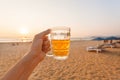 Sunset over sandy beach and one glass of cold beer in hand of happy tourist. Royalty Free Stock Photo