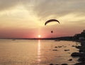 Sunset over the sea. Reflection of the sun in water. Silhouette of paraglider flying in the sky. Sunset beach in a summer evening