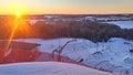 Sunset over a snow-covered ski and snowboard piste, equipped with chairlift and rope tow elevators, mesh fence and lampposts, surr Royalty Free Stock Photo