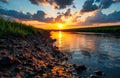 Sunset over tranquil river and pebble shoreline with glowing clouds and reflections Royalty Free Stock Photo