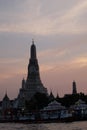 Sunset over the Wat Arun Buddhist Temple. A small passenger ferry at the pier of the Chao