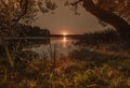 Sunset over water with reflection and sunbeams in nature in summer with trees and grass. Calm peaceful landscape with