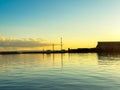 Sunset over the water with structures on the shore showing reflection in the calm surface at a port Royalty Free Stock Photo