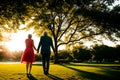 At sunset in the park, a pair of lovers walk hand in hand, their fingers interlaced, basking in the golden glow of sunset.