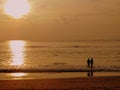 Sunset photo of a boy and girl walking into the sea while their reflection is cast on the beach behind them. Royalty Free Stock Photo