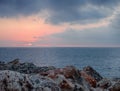 Sunset with pink and blue clouds over a calm Mediterranean sea against textured rough coastal rocks in menorca Royalty Free Stock Photo