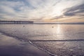 Sunset in pink color. Pacific ocean, wooden pier, and sun setting down the horizon with beautiful sun reflections on water.