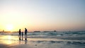 at sunset, in the rays of the sun, a married couple with a small child strolls along the beach, along the surf line Royalty Free Stock Photo