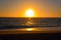 Sunset on the sandy shore of the ocean. Bright orange sun above the horizon