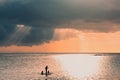 Sunset scene on coming thunderstorm background. A father with three children are paddling on two boards.Family sup paddling